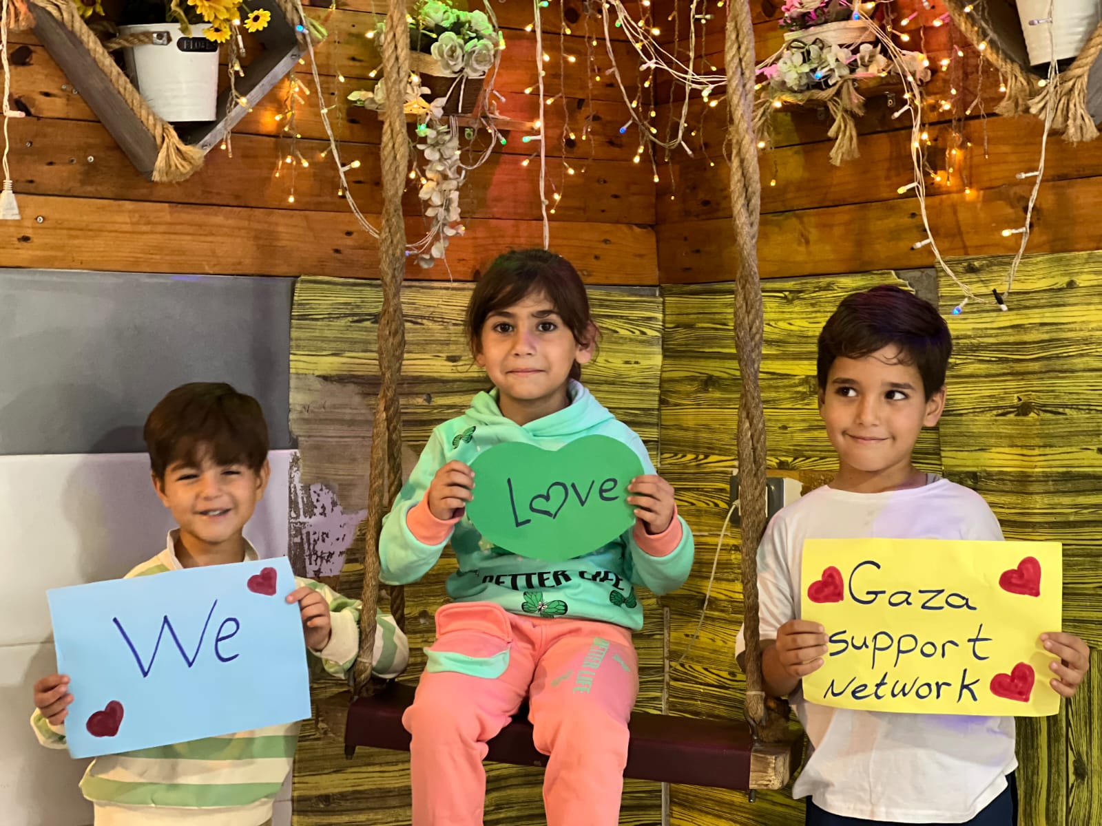 Three children holding signs that together read We Love Gaza Support Network